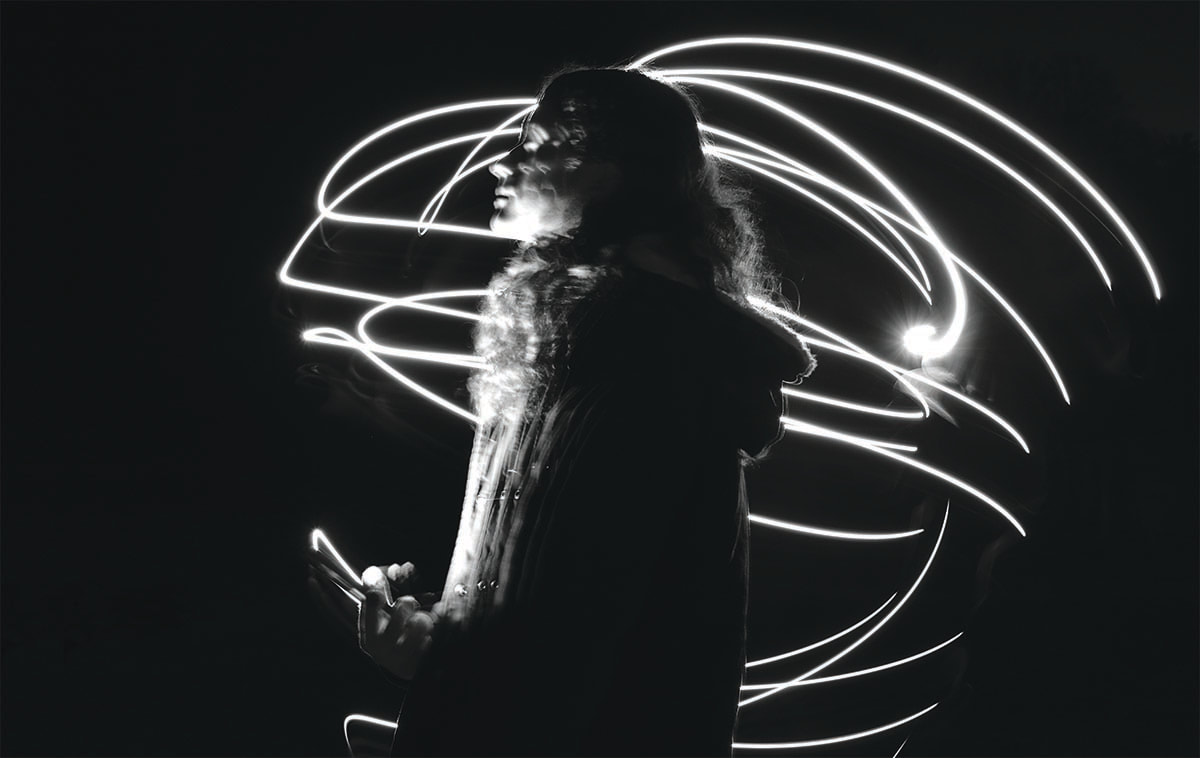 person in profile in dark space with white light swirling around them holding a cell phone